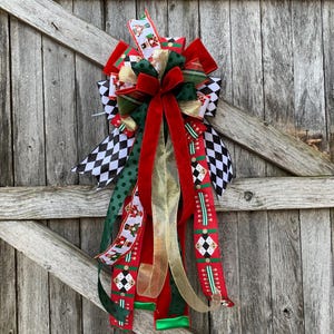 May include: A festive Christmas bow with red, green, gold, and black and white ribbons. The bow features a large red velvet bow and various patterned ribbons, including a checkerboard design. The bow is displayed against a weathered wooden background.