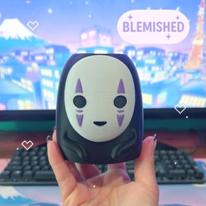 Puede incluir: Figura de No-Face en blanco y negro con detalles morados. La figura tiene forma cil&iacute;ndrica y presenta la palabra "BLEMISHED" en una burbuja de color lila claro.