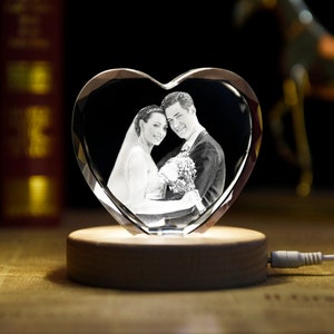 May include: A crystal heart-shaped ornament with a black and white photo of a couple inside. The ornament is on a wooden base with a light underneath it.