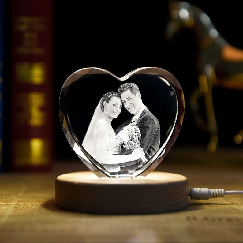 May include: A crystal heart-shaped ornament with a black and white photo of a couple inside. The ornament is on a wooden base with a light underneath it.