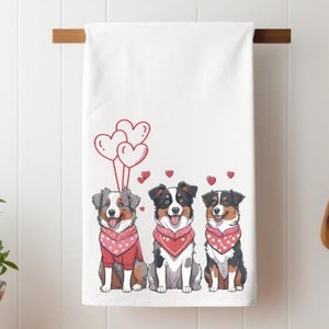 May include: Three Australian Shepherd dogs wearing red bandanas with white polka dots are sitting in a row. They are holding red heart-shaped balloons. The dogs are on a white background.