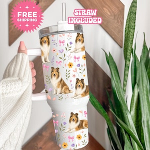 May include: A white tumbler with a handle and a straw, featuring a repeating pattern of brown and white collie dogs, pink bows, and colorful floral illustrations. The tumbler has a clear lid and a metallic straw extending from the top center.