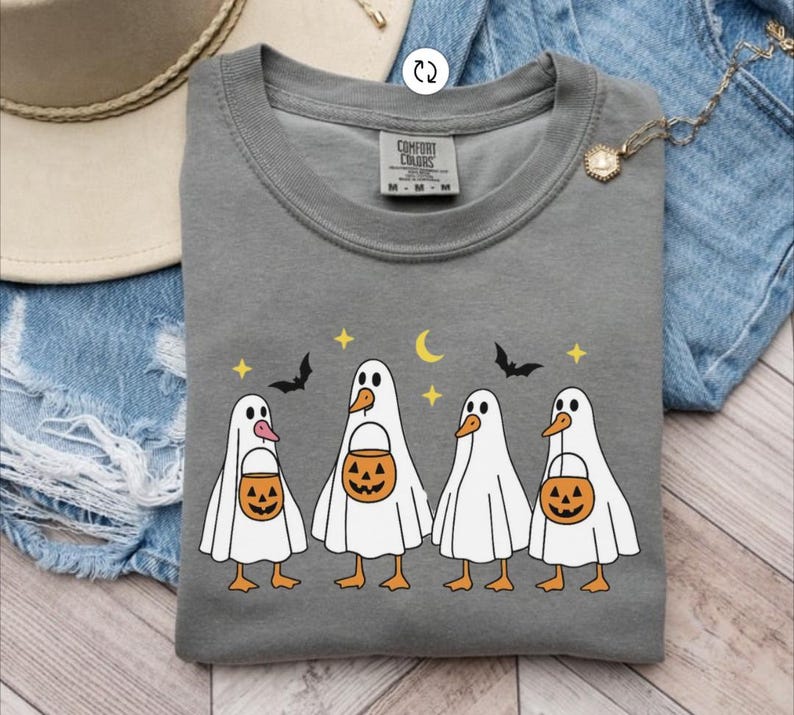 May include: A gray Comfort Colors sweatshirt featuring a Halloween-themed design. The graphic depicts four cartoon ducks dressed as ghosts, each holding a jack-o'-lantern bucket. Bats, stars, and a crescent moon complete the festive design.