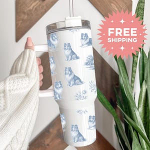 May include: White tumbler with a handle, featuring a blue and white pattern of Shetland Sheepdogs. The tumbler has a clear lid and a reusable straw. The words "FREE SHIPPING" are on a pink starburst.