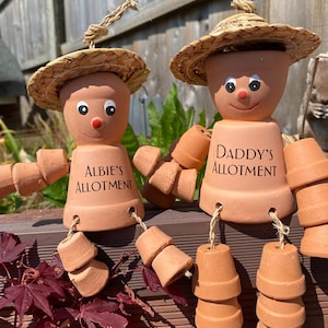 May include: Two terracotta pot figures with straw hats and rope hair. One reads "Albie's Allotment" and the other "Daddy's Allotment". The figures have painted eyes and red noses, with pot arms and legs.