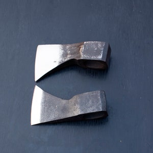 May include: Two small, hand-forged axes with wooden handles. The axes have a dark gray finish and are slightly worn.