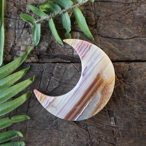 May include: A crescent moon shaped carving made from agate. The agate is a mix of white, brown, and orange colors. The carving is on a wooden surface.