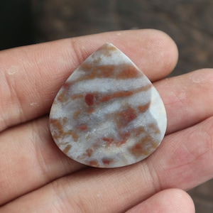 May include: A teardrop-shaped pendant made of white and brown agate with red and brown inclusions. The pendant is smooth and polished.