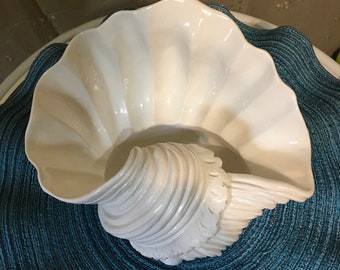 May include: White ceramic seashell bowl with a fluted rim, sitting on a blue woven placemat.