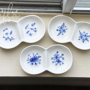May include: Four white ceramic divided dishes with blue floral designs. Each dish has two sections, and each section features a different floral pattern.