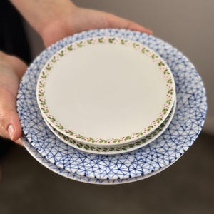 May include: A set of three ceramic mugs with a speckled, matte finish. The mugs are in shades of cream, light gray, and dark gray. Each mug has a simple, minimalist design and a rounded handle.