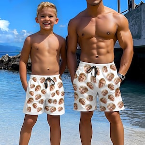 May include: Two people wearing white swim trunks with a pattern of faces printed on them. The trunks have a black drawstring.