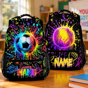 May include: Two black backpacks featuring vibrant neon paint splatter designs. The left backpack displays a soccer ball, while the right features a baseball. Both include side mesh pockets, top handles, and the word NAME in colorful lettering.