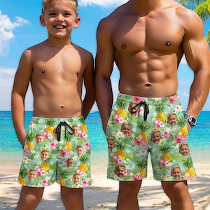 May include: Two pairs of green swim trunks with a tropical print featuring pineapples and flowers. The print also includes multiple faces of people.