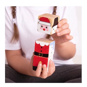 Puede incluir: Un conjunto de cuatro bloques de madera con ilustraciones de temática navideña. Los bloques representan a Papá Noel, un muñeco de nieve y un árbol de Navidad. Los bloques están pintados en rojo, blanco y verde.