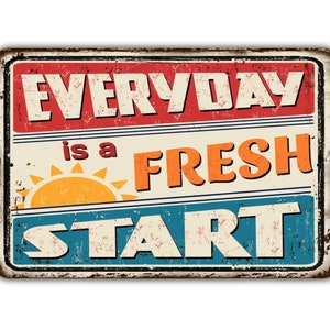 May include: A rectangular metal sign with a distressed finish. The sign features the text "EVERYDAY is a FRESH START" in red, orange, and blue, with a yellow sun graphic. The sign has a vintage, rustic aesthetic.