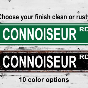Op de afbeelding: Twee metalen straatnaamborden met de tekst "CONNOISSEUR RD" in witte letters. Het bovenste bord is groen met een schone afwerking. Het onderste bord is zwart met een roestige afwerking. Kies uw afwerking schoon of roestig. 10 kleur opties.