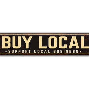 May include: A rusty metal sign with the text "BUY LOCAL" in white letters on a black background. The sign also has the text "SUPPORT LOCAL BUSINESS" in smaller white letters.