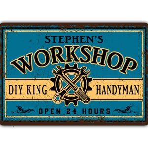 May include: A blue and yellow vintage-style sign with the text "Stephen's Workshop" and the words "DIY King" and "Handyman" on a yellow banner. The sign also includes a gear with two crossed wrenches and the text "Open 24 Hours".