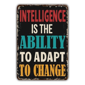 May include: A rectangular metal sign with a black background and the words "INTELLIGENCE IS THE ABILITY TO ADAPT TO CHANGE" in red, teal, white, and yellow. The sign has a distressed, vintage look.