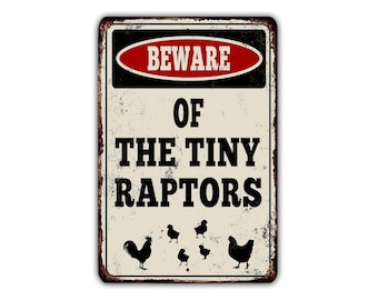 Peut inclure: Une pancarte en métal de style vintage avec un panneau d'avertissement qui indique "Attention aux petits raptors". La pancarte a une bordure rouge et noire avec du texte blanc. Il y a cinq silhouettes noires de poulets sur la pancarte.