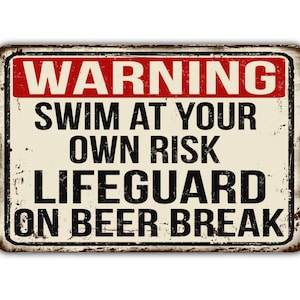 Könnte beinhalten: Ein Vintage-Schild aus Metall mit einer Warnung: "WARNING SWIM AT YOUR OWN RISK LIFEGUARD ON BEER BREAK". Das Schild hat einen abgenutzten, rostigen Look und ist in Schwarz und Rot auf cremefarbenem Hintergrund gedruckt.