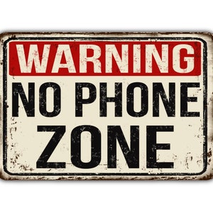 May include: A vintage-style metal sign with a warning message: "WARNING NO PHONE ZONE". The sign has a red background for the word "WARNING" and a white background for the rest of the text. The sign has a distressed, rusty look.