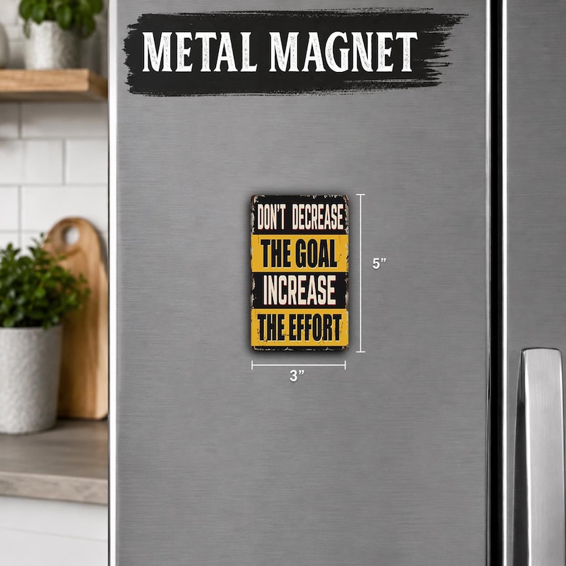 a small metal magnet with a motivational quote on it, placed on the surface of a refrigerator.