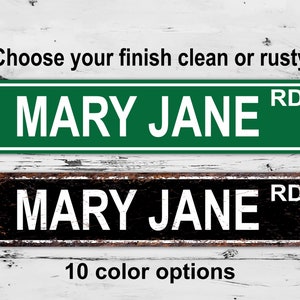 May include: Two rectangular street signs with the text "MARY JANE RD". One sign is green with white text, the other is black with white text. The text "Choose your finish clean or rusty" and "10 color options" are also present.