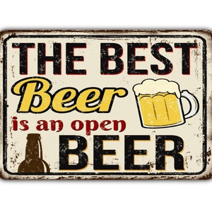 Könnte beinhalten: Ein Vintage-Schild aus Metall mit einem abgenutzten, rostigen Look. Es trägt die Aufschrift "The Best Beer is an Open Beer" mit einem Cartoon-Bild einer Bierflasche und einem Glas Bier.
