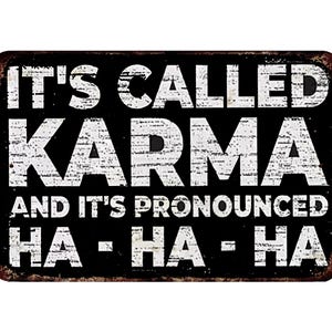 Könnte beinhalten: Rechteckiges schwarzes Metallschild mit weißem, verwittertem Text: "IT'S CALLED KARMA AND IT'S PRONOUNCED HA - HA - HA". Das Schild hat einen verwitterten, rostigen Rand.