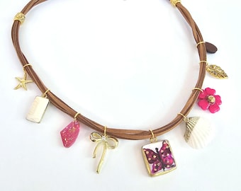 May include: A multi-strand brown cord necklace featuring various gold-toned charms including a starfish, a bow, a butterfly square pendant, a white seashell, a pink flower, a leaf, and several resin-style geometric pieces with gold accents.