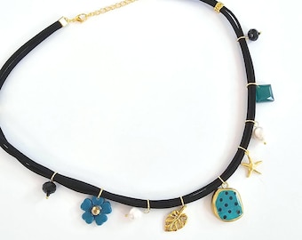 May include: Black choker necklace with gold accents and various charms. Charms include a blue flower, gold leaf, turquoise pendant with black dots, and a gold starfish. Additional charms are a green square and black beads.