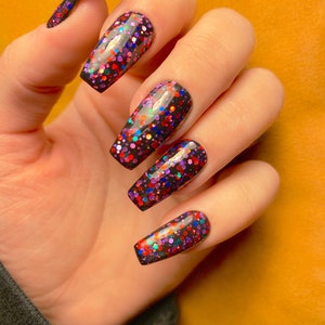May include: Close-up of a hand with long, black, coffin-shaped nails. The nails are covered in a black base with multi-colored glitter.