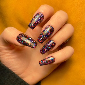 May include: Close-up of a hand with long, black coffin-shaped nails. The nails are covered in a black base coat with multi-colored glitter.