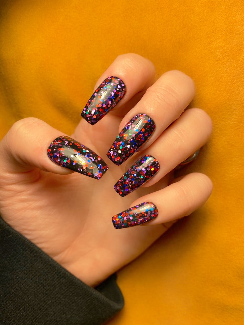 May include: Close-up of a hand with long, black coffin-shaped nails. The nails are covered in a black base coat with multi-colored glitter.