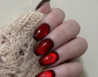 May include: Close-up of a hand with five red nails with a shimmery finish. The nails are long and oval-shaped.