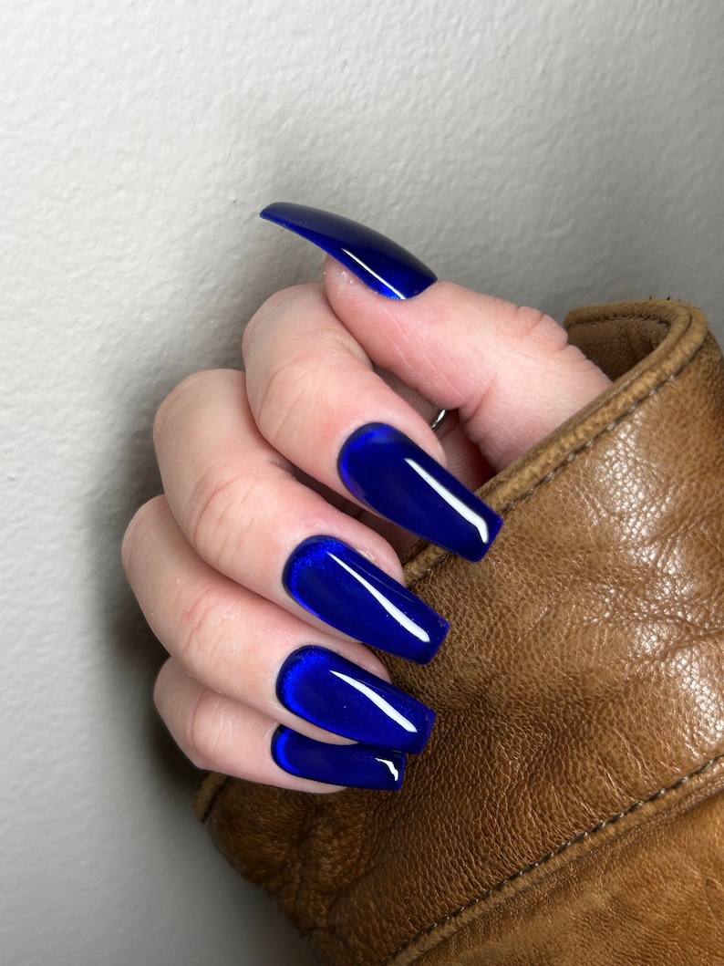 May include: Close-up of a hand with long, blue, coffin-shaped nails. The nails have a glossy finish and a slight shimmer.