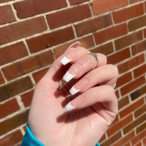May include: Close-up of a hand with white french manicured nails. The nails are long and oval shaped. The hand is wearing a silver ring.