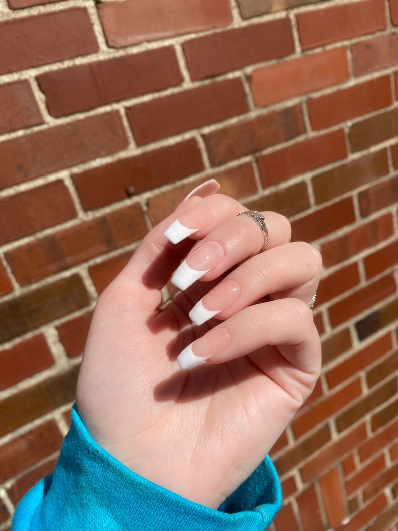May include: Close-up of a hand with white french manicured nails. The nails are long and oval shaped. The hand is wearing a silver ring.