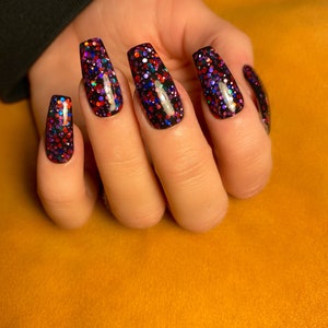 May include: Close-up of a hand with long, black coffin-shaped nails with multi-colored glitter polish.