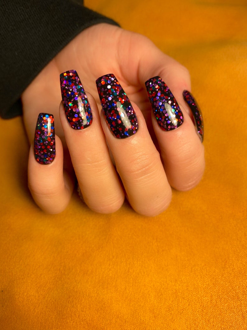 May include: Close-up of a hand with long, black coffin-shaped nails with multi-colored glitter polish.