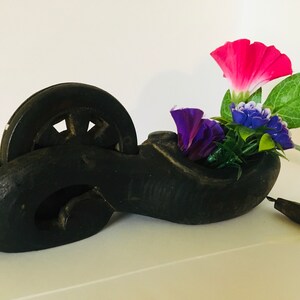 May include: A black wooden line marking tool with a spool and a handle. The tool is used for marking lines on surfaces. The tool is decorated with a small bouquet of pink and purple flowers.