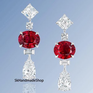 May include: Pair of drop earrings with a large oval ruby gemstone, complemented by diamond shapes and a pear-shaped diamond. The earrings are set in silver metal, offering a luxurious appearance.