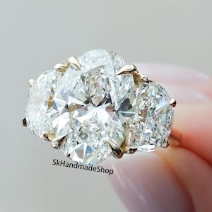 May include: A gold ring with three large oval-shaped diamonds. The center diamond is the largest and the two side diamonds are smaller. The ring is set in a prong setting.