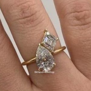 Peut inclure: Une bague en or ornée d'un diamant en forme de poire et d'un diamant taille émeraude. La bague a un anneau fin et est sertie de deux pierres précieuses claires et étincelantes. La bague est portée au doigt.