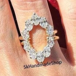 May include: A gold ring with a halo setting of small round diamonds. The ring is set with a large oval-shaped diamond in the center. The ring is on a finger with red nail polish.