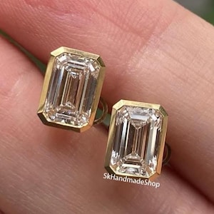 Op de afbeelding: Een paar goudkleurige oorstekers met heldere, smaragdgeslepen edelstenen. De oorbellen zijn rechthoekig met een gouden rand. De tekst "SkHandmadeShop" is zichtbaar aan de rechterkant van de afbeelding.