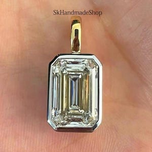May include: A rectangular pendant with a large, clear, emerald-cut gemstone. The gemstone is set in a silver-colored bezel with a gold-colored bail. The text "SkHandmadeShop" is visible.