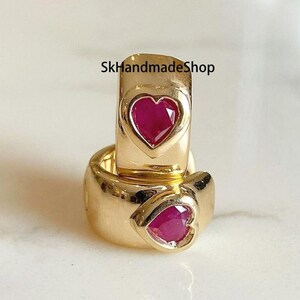 Puede incluir: Un par de pendientes de aro de oro con una piedra preciosa en forma de corazón de rubí en cada uno. Los pendientes están apilados uno encima del otro. El texto "SkHandmadeShop" es visible en el fondo.